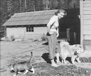 A white woman with her hands on her hips with a dog and cat at her feet